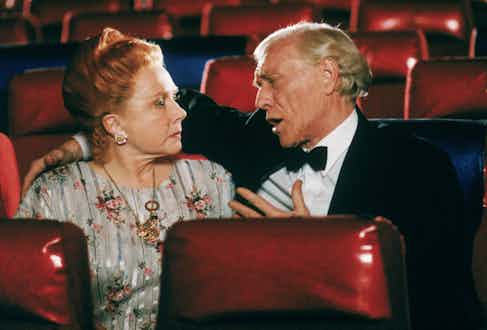 Medium shot of Richard Harris as Frank, wearing tuxedo, facing and with arm around Shirley MacLaine as Helen Cooney; both seated in empty theater. Photo by Warner Bros./Getty Images.