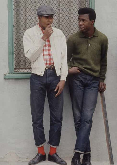 Preppy rebels from Los Angeles' Watts community purposefully dressed well to diffuse racial stereotyping in the 1960s. Here, one wears a peaked cap with a casual, considered look that includes an off-white blouson and turn-up jeans.