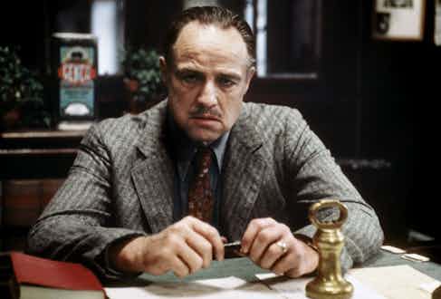 Don Vito Corleone sporting a rustic tweed single-breasted suit with a light blue shirt and red printed tie.