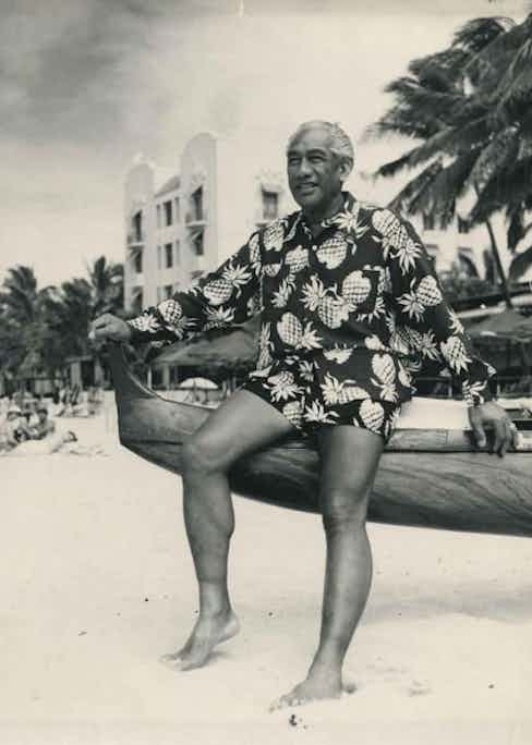 Surfing legend Duke Kahanamoku wears a long sleeve pineapple motif Hawaiian shirt with matching shorts on a beach in Hawaii, circa 1945.