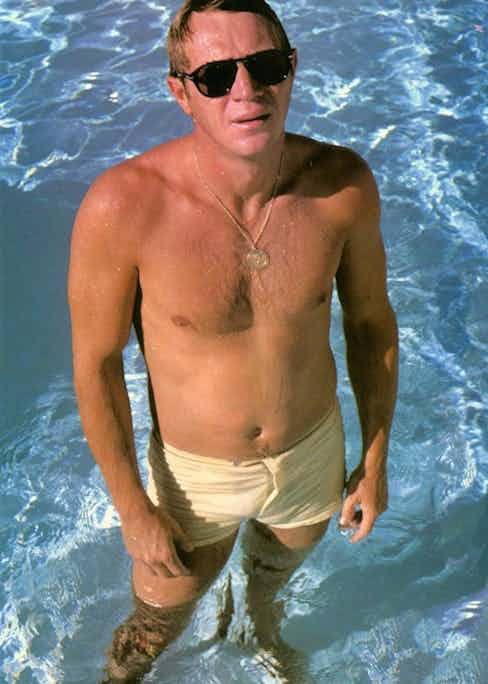 Steve McQueen wearing swim shorts and his signature Persol sunglasses, circa 1960s.